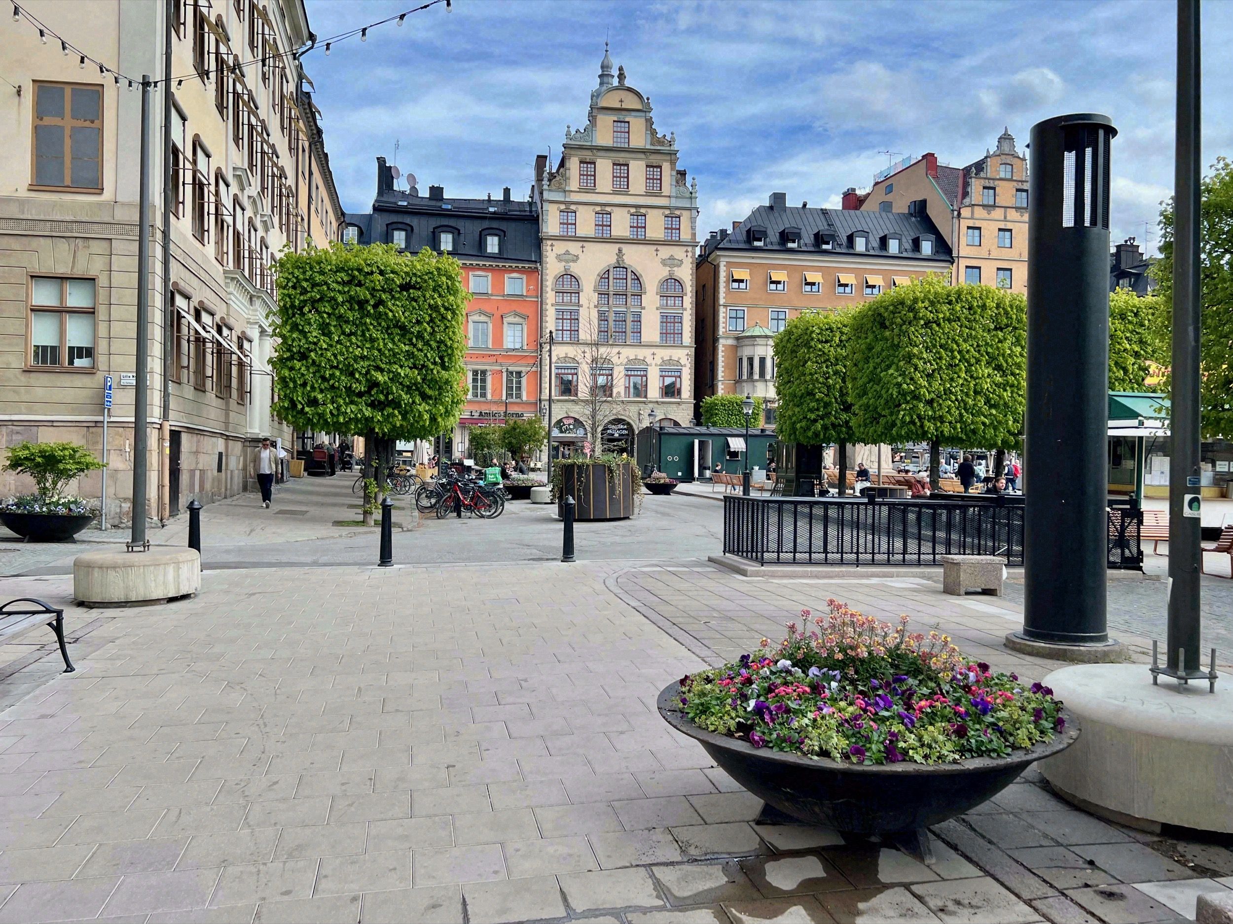 Gepflasterter Platz in Gamla Stan mit bunten Historismusfassaden, beschnittenen Bäumen und Blumenschmuck.