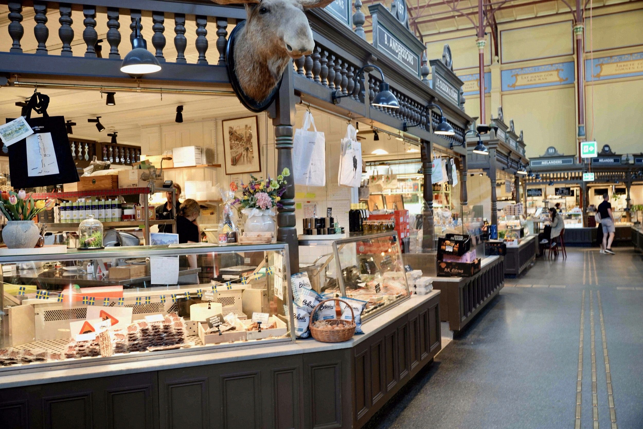 Blick in die historische Markthalle Östermalms Saluhall mit prunkvollen Delikatessenständen und präpariertem Elchkopf.