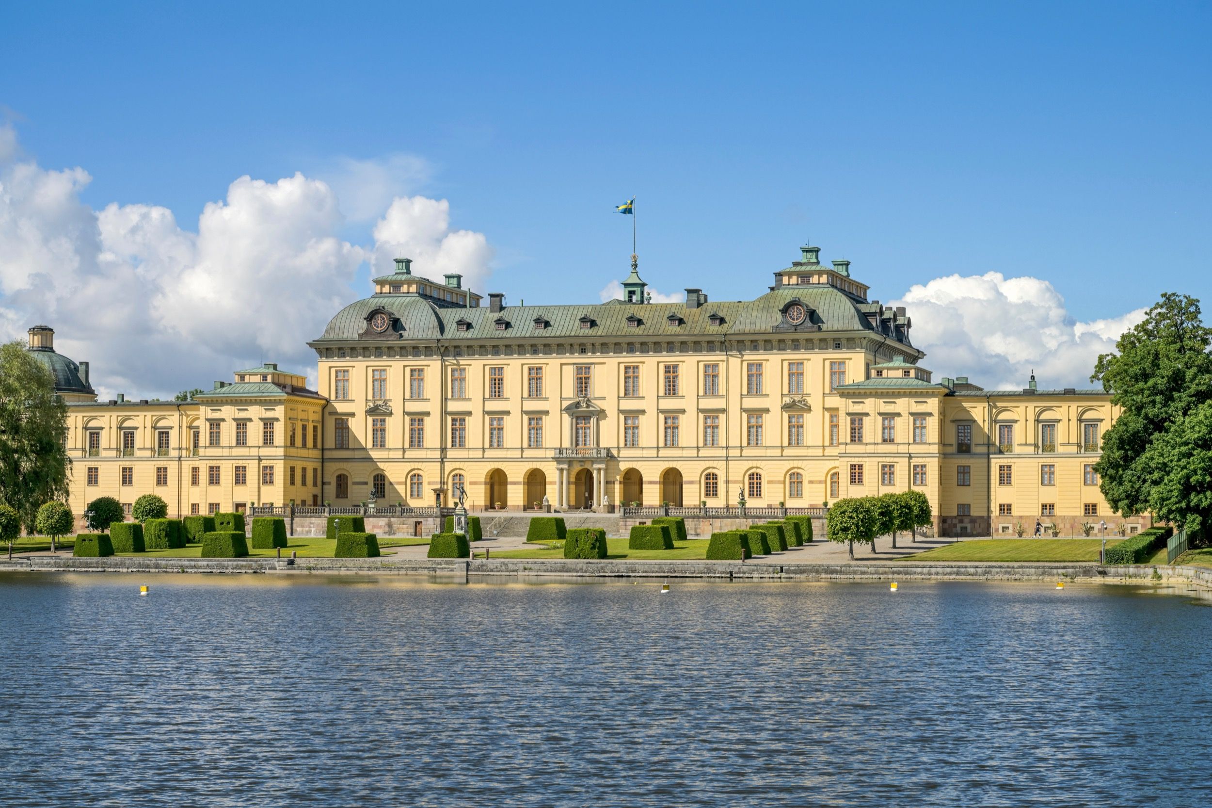 Das königliche Schloss Drottningholm mit gelbem Anstrich vom Wasser aus, eines der wichtigsten Schlösser im Großraum Stockholm.