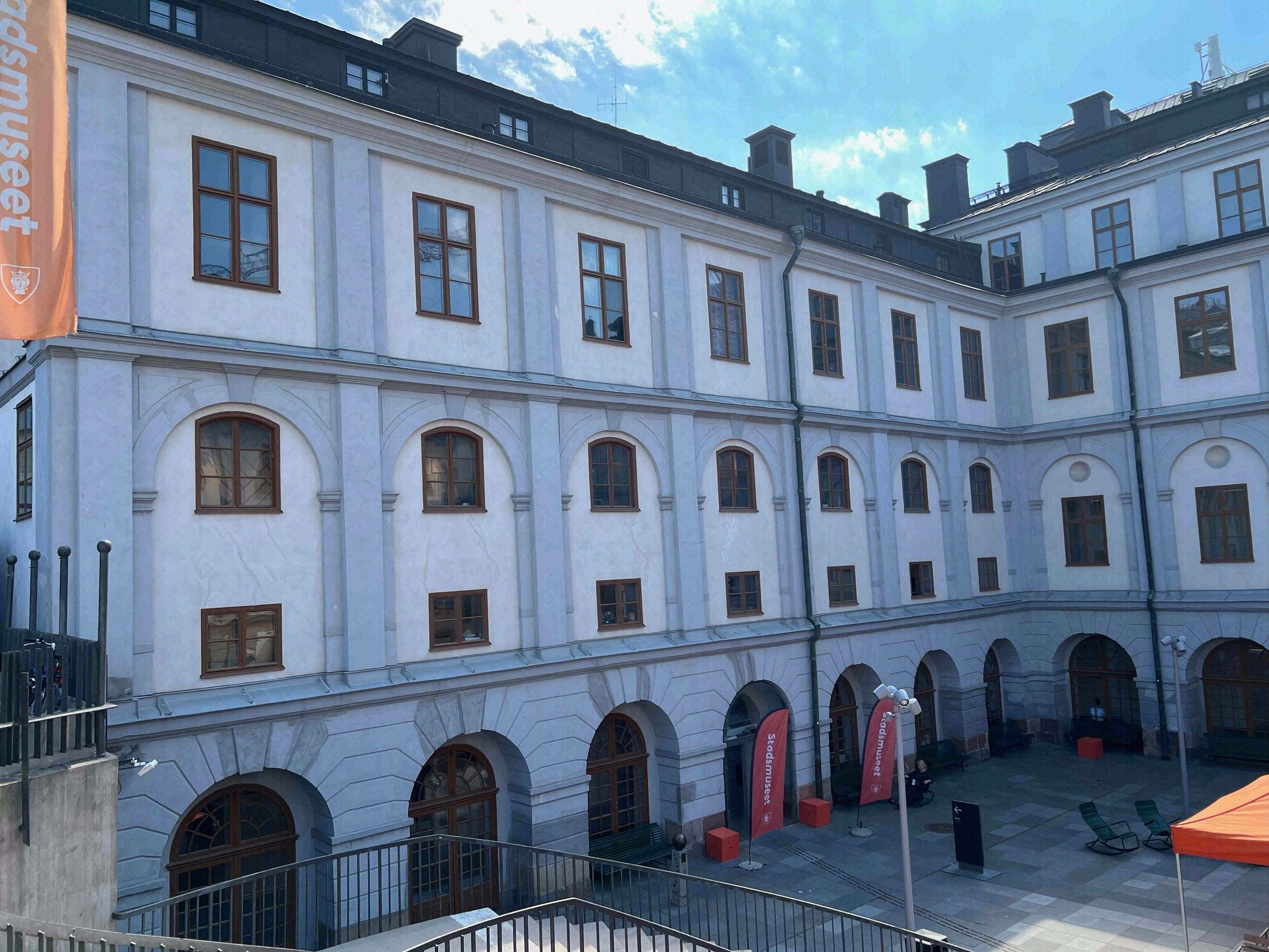 Barocker Innenhof des Stockholmer Stadtmuseums (Stadsmuseet) mit orangefarbenem Banner und Außenbestuhlung.