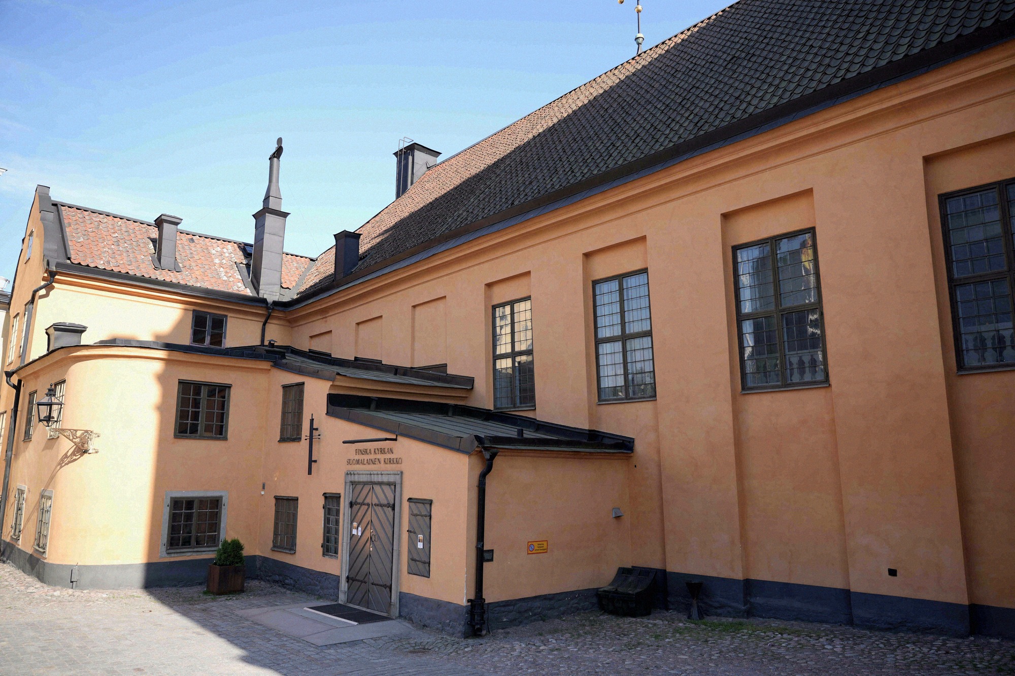 Side entrance of Finska kyrkan (the Finnish Church) in Gamla Stan, with orange render and a sign reading 'Finska kyrkan – Blomsterzon-gallerij'.