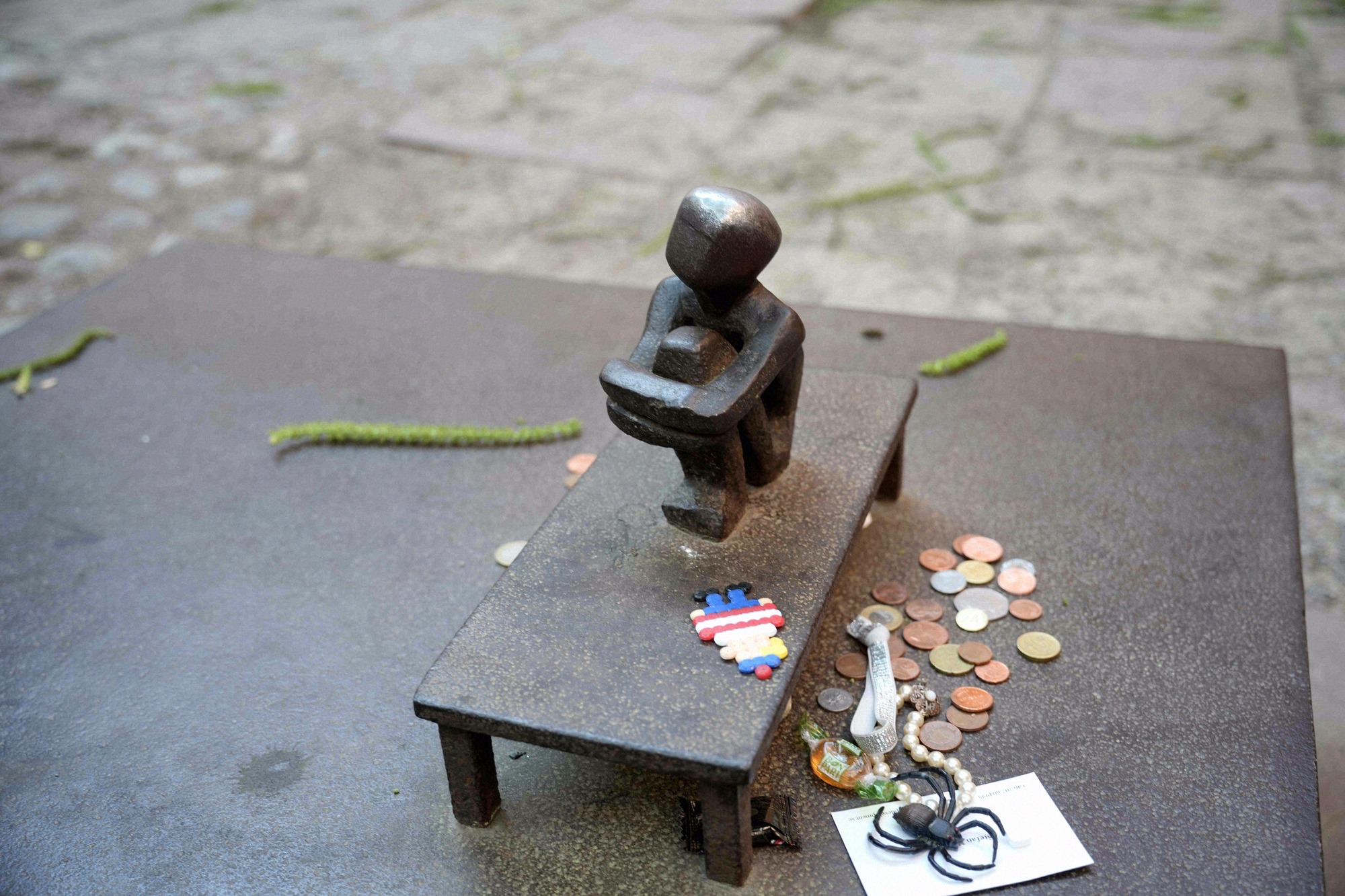 The Järnpojke in the courtyard of the Finnish Church, with coins left by visitors. Close-up of the small bronze Järnpojke sculpture with coins and small offerings