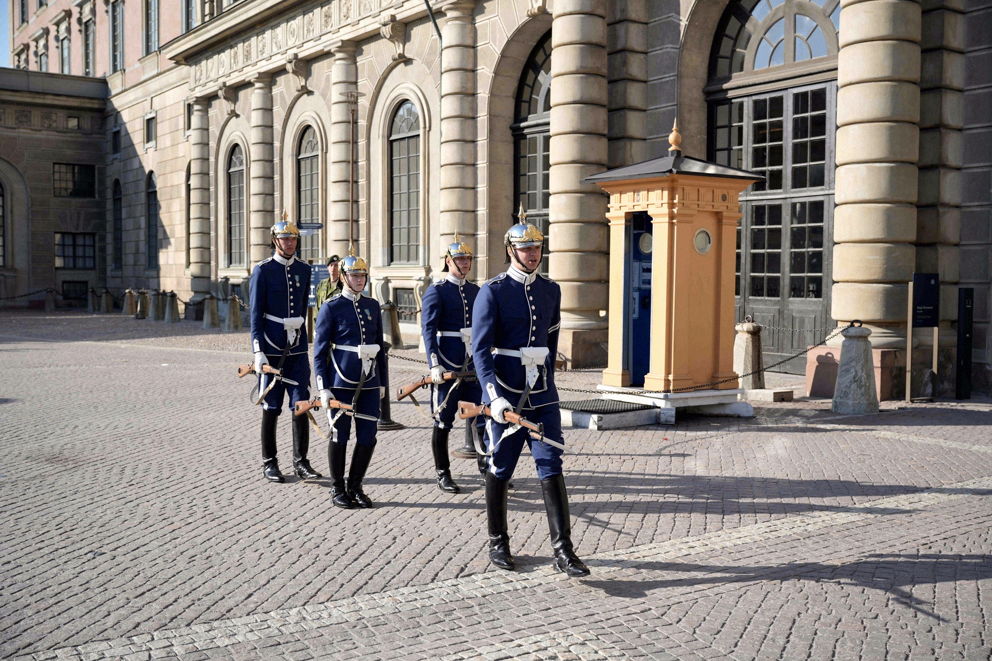 Changing of the Guard at the Royal Palace: soldiers in blue dress uniform in the courtyard. Four soldiers in blue dress uniform march during the Changing of the Guard across the palace courtyard