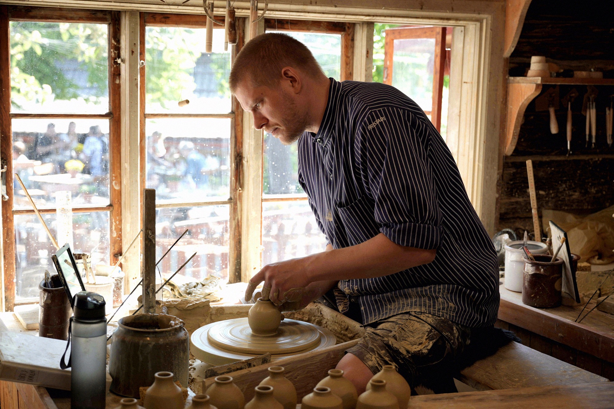 A potter at the wheel in one of the historic workshops. A potter shapes a vessel on the wheel in a historic wooden workshop
