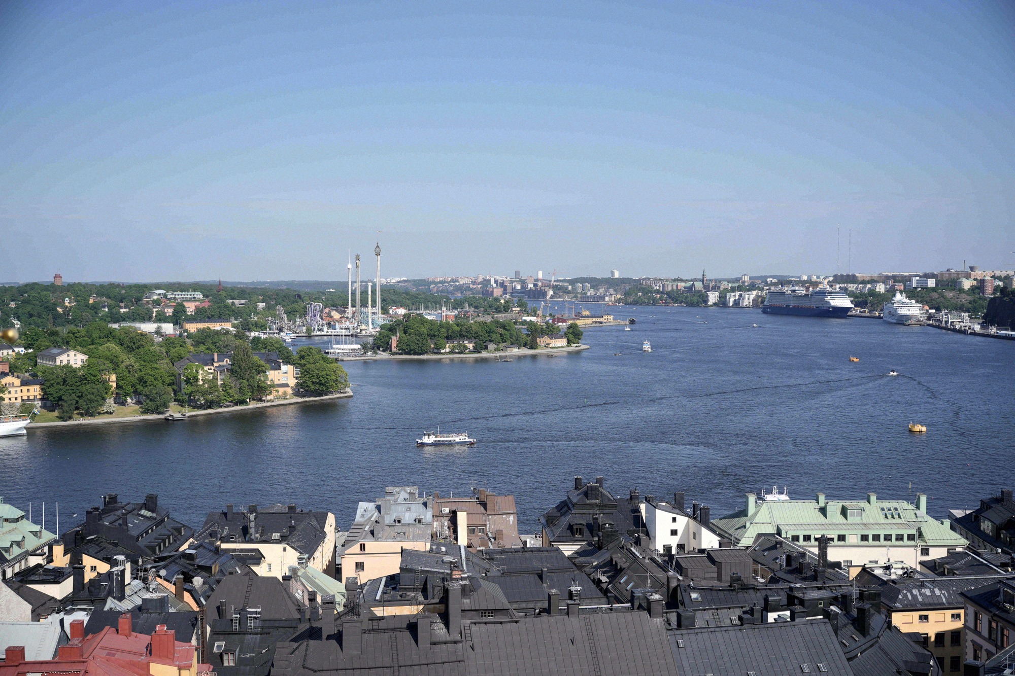 View from the tower of the German Church across the rooftops of Gamla Stan towards Djurgården, with Gröna Lund and the surrounding waters.